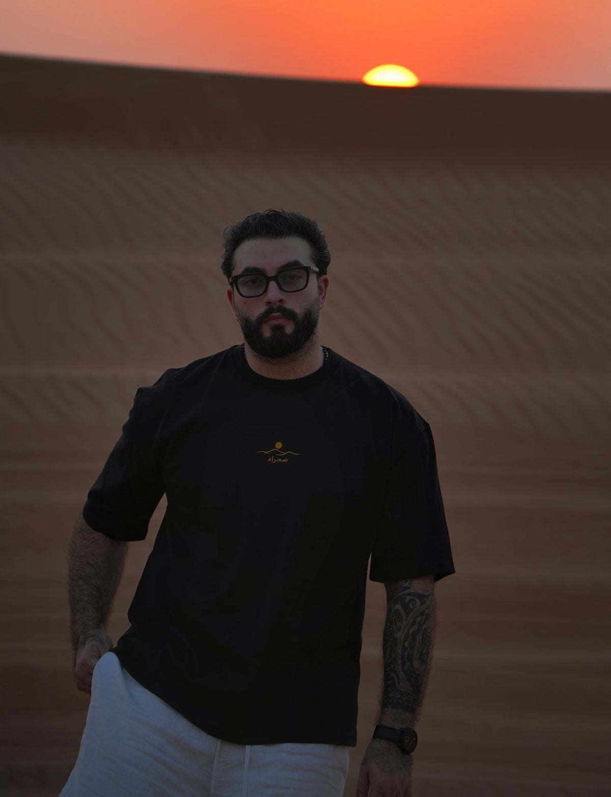 The Al Quaa Galaxy tee worn facing the last light, embroidered chest mark catching the gold. Male model is 182 cm, wearing L in the Oversized fit.
