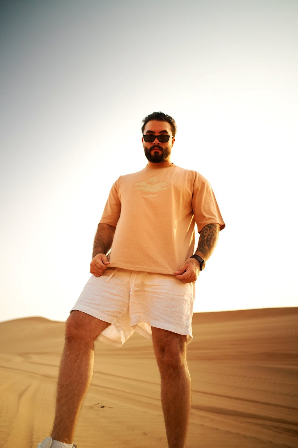 The Empty Quarter tee worn standing on a dune at golden hour. Male model is 182 cm, wearing L in the Oversized fit.
