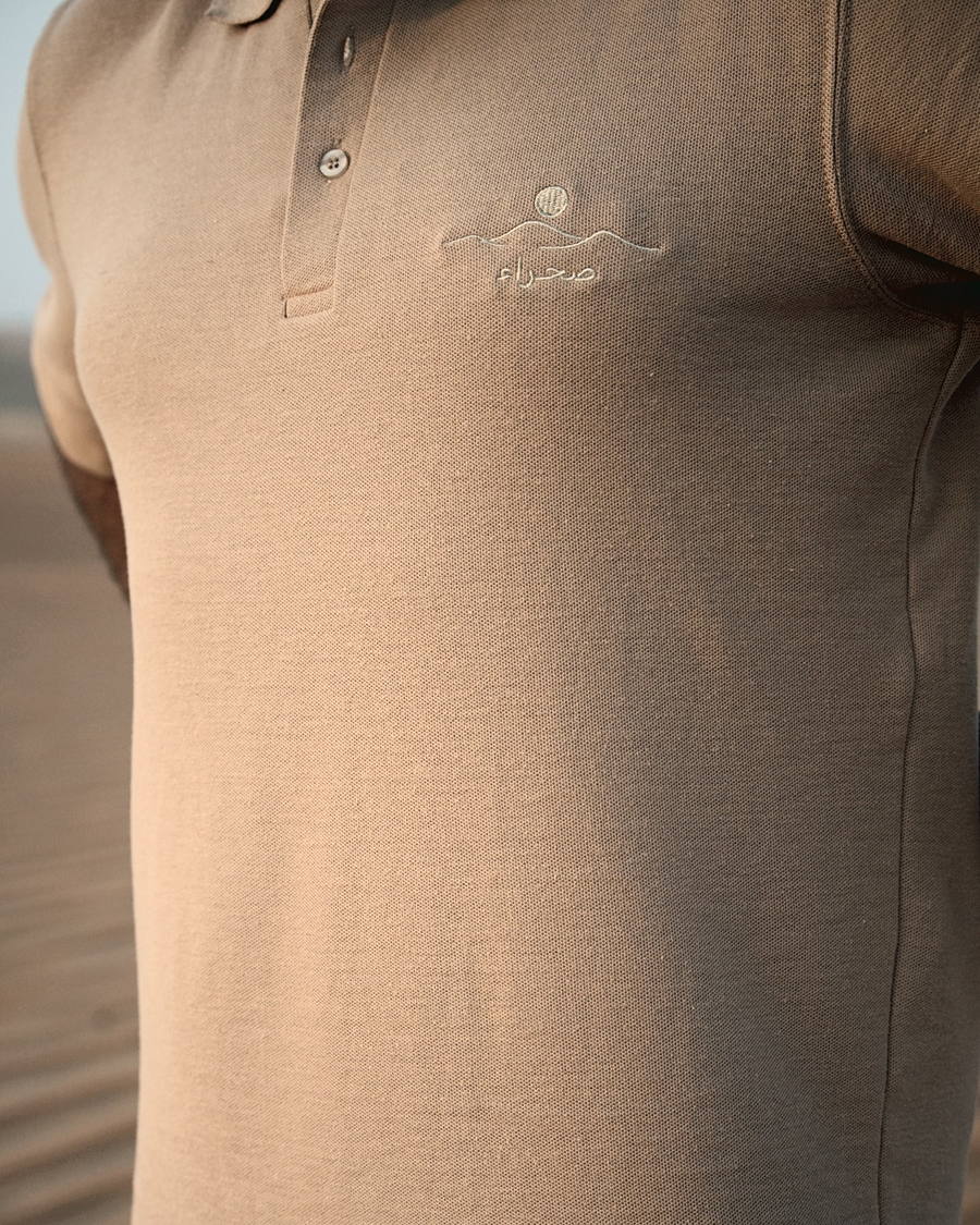 The Sahra Polo, chest detail — the embroidered صحراء mark and the buttoned placket on 240gsm piqué