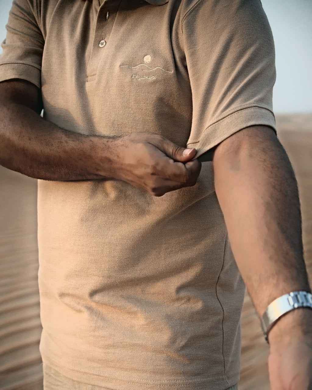 The Sahra Polo held at the hem — the weight of the piqué and the side seam